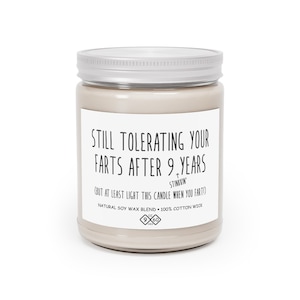 May include: A beige candle jar with a silver lid. The label reads "STILL TOLERATING YOUR FARTS AFTER 9 YEARS (BUT AT LEAST LIGHT THIS CANDLE WHEN YOU FART!)" with the text "STINKKIN'" above the parentheses. The label also includes the text "NATURAL SOY WAX BLEND - 100% COTTON WICK" and a logo with the numbers "9 x 60".
