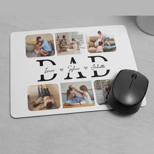 May include: A white rectangular mousepad with a black wireless mouse. The mousepad features six family photos and the word "DAD" in large black letters, with the names "Laura", "Sylvia", and "Juliette" below.