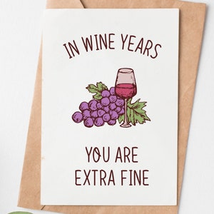 May include: A greeting card with a hand-drawn illustration of a glass of red wine and a bunch of grapes. The text on the card reads "In wine years you are extra fine."