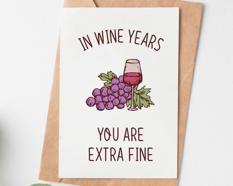 May include: A greeting card with a hand-drawn illustration of a glass of red wine and a bunch of grapes. The text on the card reads "In wine years you are extra fine."