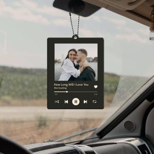 May include: Black rectangular car air freshener with a photo of a couple embracing. The design mimics a music player interface, displaying the song title "How Long Will I Love You" by Ellie Goulding.
