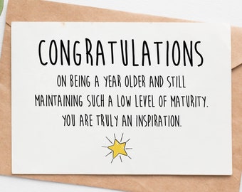 May include: A white card with black text that reads "Congratulations on being a year older and still maintaining such a low level of maturity. You are truly an inspiration." A yellow star with rays is at the bottom of the card.