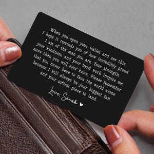 May include: A black wallet card with white text held by a person. The card has a heartfelt message that reads, "When you open your wallet and see this..." The card is a sentimental gift.