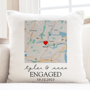 May include: White throw pillow with a map of Newark, New Jersey, featuring a red heart marking a location. The text "tyler & anna ENGAGED 10.12.2023" is printed below the map.