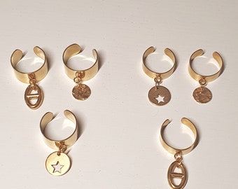 Puede incluir: Seis anillos dorados con dijes colgantes. Los dijes incluyen una estrella, un círculo con una estrella recortada y una letra "O" con un círculo recortado. Los anillos están dispuestos sobre una superficie blanca. El texto "MADE MOIS'L RÊVE" es visible en la parte inferior de la imagen.