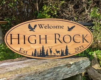 Puede incluir: Bienvenido a High Rock, establecido en 2023. Un letrero ovalado de madera con texto negro y una silueta de una escena de bosque con ciervos y águilas.