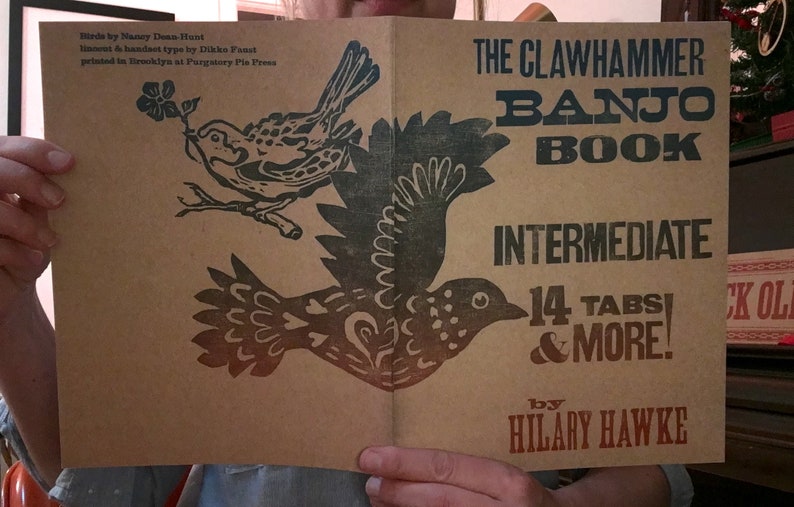 以下が含まれることがあります： クローハンマー・バンジョー・ブック：中級、14のタブ譜とその他、ヒラリー・ホーク著。表紙は茶色の背景に、花が咲いた枝にとまっている黒い鳥と、飛んでいる黒い鳥の2羽が描かれている。タイトルは青と赤の文字で書かれている。