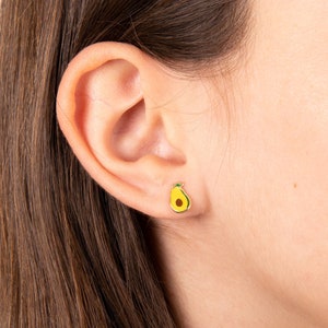 May include: A pair of gold-tone earrings featuring a small avocado design. The avocado is yellow with a green pit.