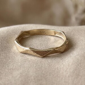 May include: A thin gold ring with a faceted, geometric band design. The interior of the band is clearly stamped with the text 14K, indicating the gold purity. The ring features a series of angled, flat surfaces that create a repeating pattern.