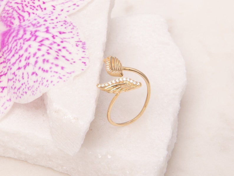 May include: A gold ring with two wings adorned with small clear stones. The wings are connected by a thin band.
