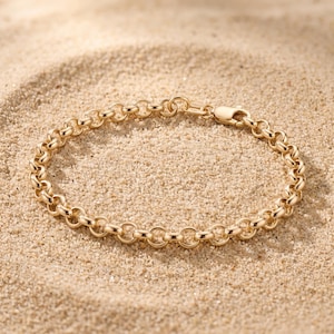 May include: A gold rolo chain bracelet featuring a series of polished, round, interlocking links. The bracelet is secured with a lobster claw clasp and includes a small rectangular tag near the closure, which is stamped with the text 14K.