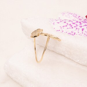 May include: A gold ring with a delicate wing design. The ring is set against a white background with a pink orchid flower.
