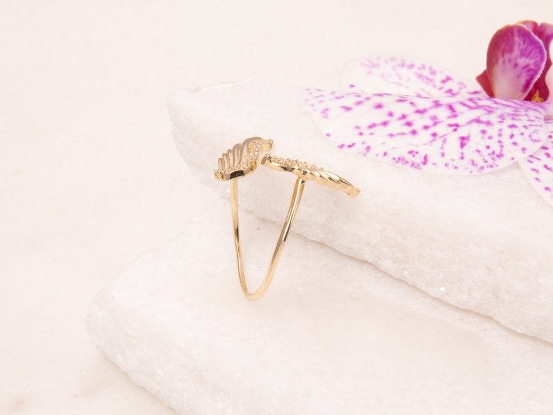 May include: A gold ring with a delicate wing design. The ring is set against a white background with a pink orchid flower.