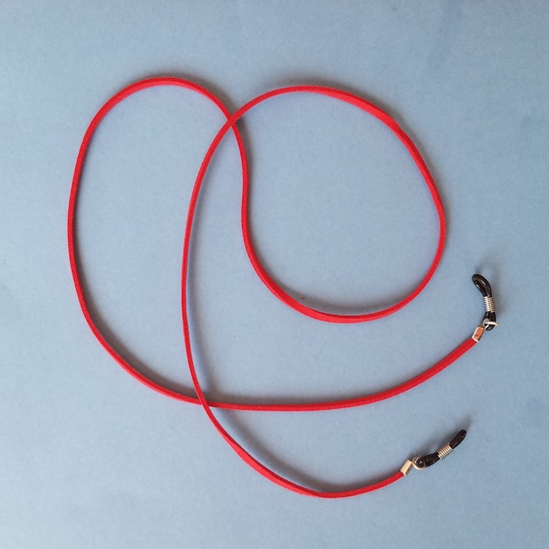 May include: Red glasses chain with black metal ends. The chain is made of a soft, flexible material and is designed to hold glasses securely around the neck.