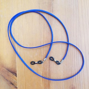 May include: A pair of blue glasses retainers with black rubber ends. The retainers are lying on a wooden surface.