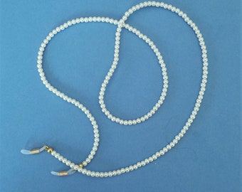 May include: White pearl glasses chain with gold-toned clasps. The chain is made of faux pearls and is designed to hold glasses.