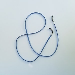May include: A blue eyeglass chain with silver clasps. The chain is made of a thin, flexible material and is designed to hold eyeglasses securely around the neck.