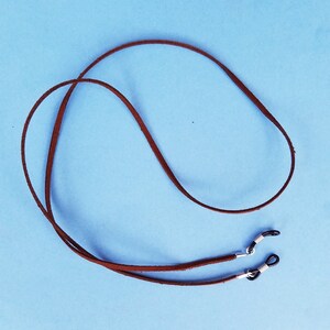 May include: A brown leather eyeglass chain with silver metal clasps. The chain is on a light blue background.