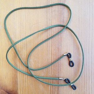 May include: A pair of green suede glasses straps with black metal ends. The straps are tied together in a knot.