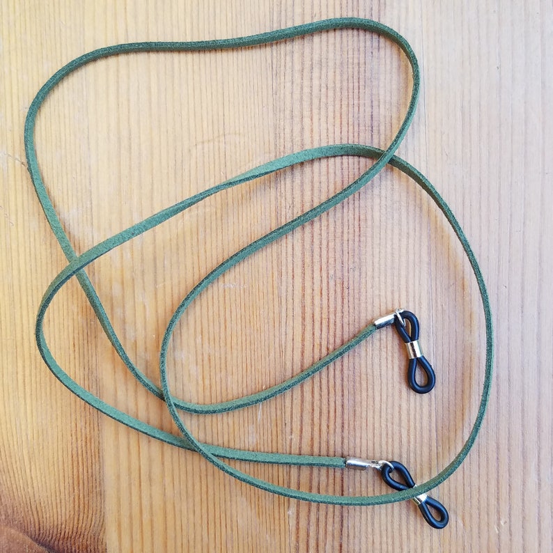 May include: A pair of green suede glasses straps with black metal ends. The straps are tied together in a knot.