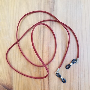 May include: A burgundy leather eyeglass chain with black rubber ends. The chain is looped and ready to be worn.
