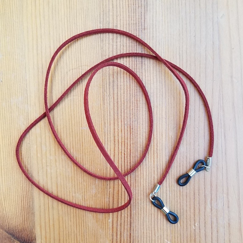 May include: A burgundy leather eyeglass chain with black rubber ends. The chain is looped and ready to be worn.