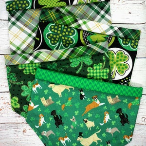 May include: A stack of four green and black dog bandanas with a shamrock pattern. The top bandana has a plaid pattern with gold accents. The bottom bandana features a green background with a pattern of dogs and shamrocks.