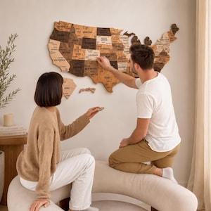 Peut inclure: Une grande carte murale en bois des États-Unis aux tons variés, présentant des frontières d'États découpées au laser et des noms d'États gravés. La carte est composée de différentes nuances de bois brun et fixée au mur.