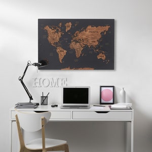 Può includere: Una scrivania bianca con due cassetti e un computer portatile nero sopra. Una sedia bianca con gambe in legno è davanti alla scrivania. Una mappa del mondo con uno sfondo grigio scuro e continenti marroni è appesa al muro sopra la scrivania. La parola "HOME" è scritta in lettere bianche sul muro sotto la mappa.