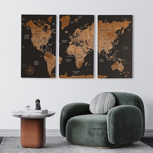 May include: Three wooden world maps with a black background and a brown map design. The maps are mounted on a white wall above a green velvet armchair, a marble-topped table, and a grey rug.