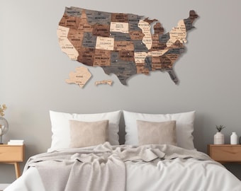 May include: A wooden map of the United States with each state labeled. The map is mounted on a light gray wall above a white bed with a beige blanket and two pillows.
