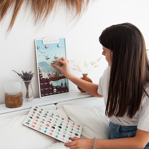 May include: A wooden board with a map of the United States National Parks. Each park is represented by a small, colorful icon. A person is holding a separate board with the same icons, but they are larger and can be used to mark which parks they have visited.