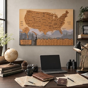 May include: A rectangular wall map of the United States made of cork, featuring labeled states and national parks. The map includes a mountain and forest graphic at the bottom, with the text National Park Adventures printed in a rectangular box.