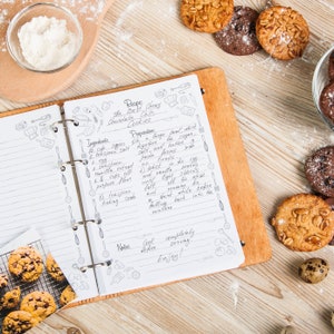 May include: A handwritten recipe for chocolate chip cookies on a notebook with a wooden cover. The recipe includes ingredients, preparation instructions, and notes. The notebook is open and lying on a wooden table with a bowl of flour and chocolate chip cookies scattered around.