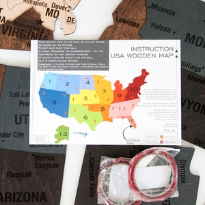 May include: A close-up of a USA wooden map puzzle with instructions on how to assemble it. The map is divided into 14 pieces, each with a number on it. The instructions include a diagram showing the correct placement of each piece. The map is made of wood and has a natural finish. The instructions are printed on a white sheet of paper.