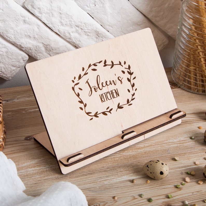 May include: A wooden cookbook stand with a personalized inscription that reads "Joleen's Kitchen" surrounded by a decorative floral wreath.