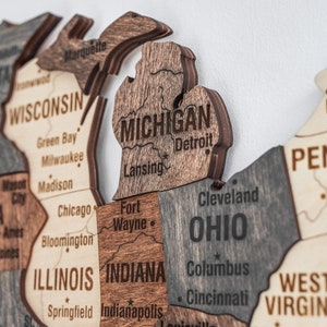 May include: A wooden map of the United States with the states of Michigan, Ohio, Indiana, Illinois, Wisconsin, West Virginia, and Pennsylvania highlighted. The states are labelled with their names and major cities.
