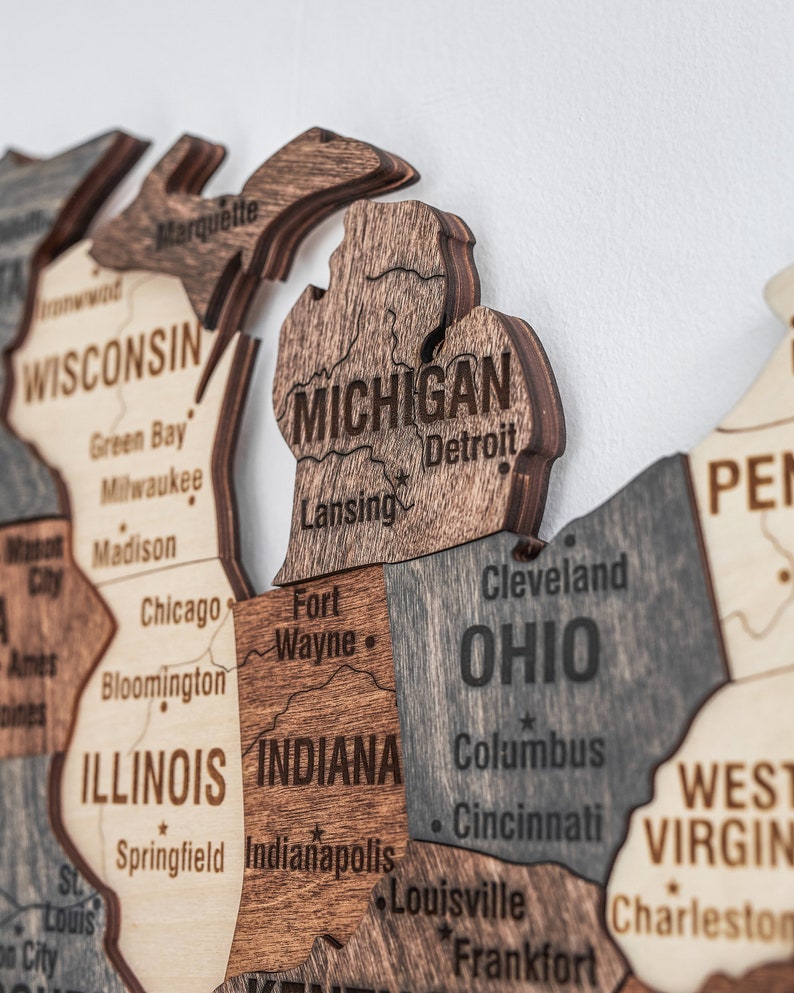 May include: A wooden map of the United States with the states of Michigan, Ohio, Indiana, Illinois, Wisconsin, West Virginia, and Pennsylvania highlighted. The states are labelled with their names and major cities.