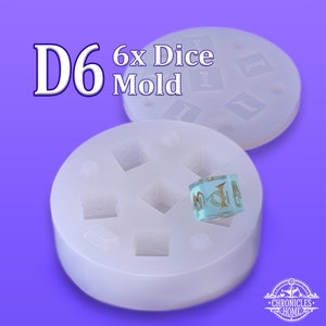 May include: A white silicone mold for making six dice. The mold has six individual cavities shaped like dice. A clear blue dice with gold lettering is sitting on top of the mold.
