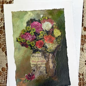 May include: A rectangular greeting card featuring a mixed-media collage of a floral bouquet with pink, red, yellow, and white flowers. The base includes torn book pages with the text The pretties and a signature in the bottom right corner.