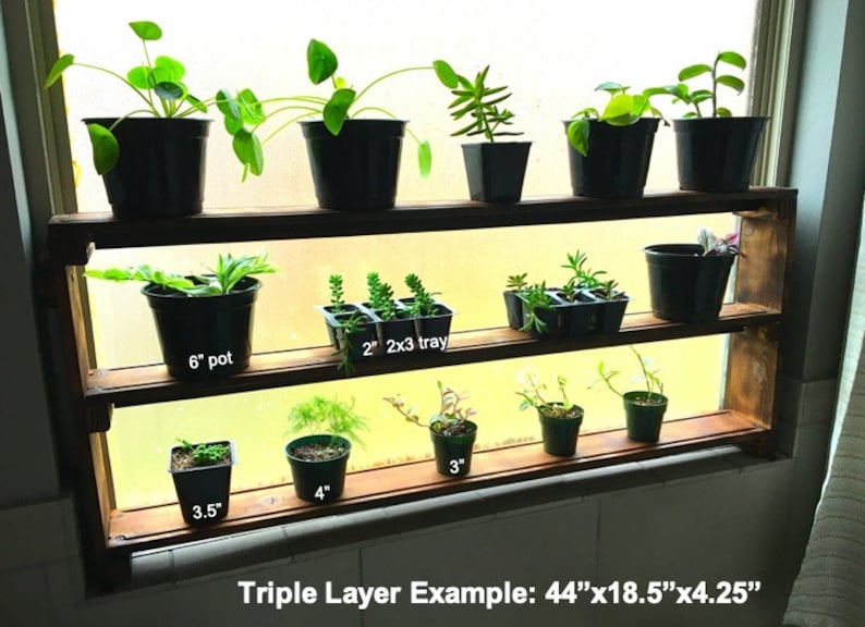 May include: A wooden shelf unit with three tiers, designed to hold potted plants. The shelf is 44 inches long, 18.5 inches wide, and 4.25 inches deep. The shelf is filled with various plants in different sized pots, including a 6-inch pot, a 3.5-inch pot, a 4-inch pot, and a 2-inch by 3-inch tray.
