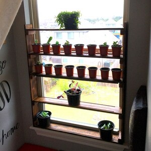 May include: Five-layer wooden shelf unit with plants in pots, mounted on a window frame. The shelf is 34 inches wide by 39 inches tall and 4.25 inches deep.