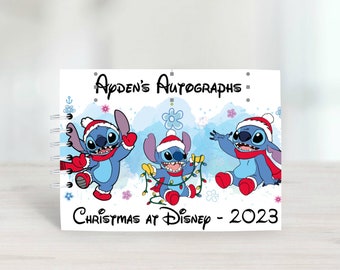 Puede incluir: Un libro de autógrafos blanco con un personaje azul Stitch que lleva un gorro de Papá Noel. El libro tiene el texto "Ayden's Autographs - Christmas at Disney - 2023" en la portada.