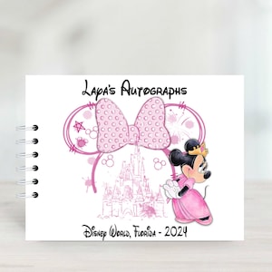 Può includere: Un libro di autografi rosa e bianco con un fiocco rosa, un castello rosa e una Minnie Mouse rosa con una corona. Il libro dice "Lapa's Autographs" e "Disney World, Florida - 2024".