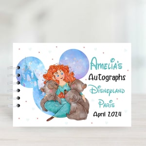 Può includere: Un libro di autografi bianco con un design a forma di testa di Topolino blu e viola. Il libro presenta un'immagine di cartone animato di una ragazza dai capelli rossi con tre orsi marroni. Il testo sul libro recita "Amelia's Autographs Disneyland Paris April 2024".