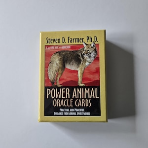 May include: A deck of "Power Animal Oracle Cards" by Steven D. Farmer, Ph.D. The box is yellow with a coyote illustration on a red background. Text includes "A 44-CARD DECK with GUIDEBOOK" and "PRACTICAL AND POWERFUL GUIDANCE FROM ANIMAL SPIRIT GUIDES."