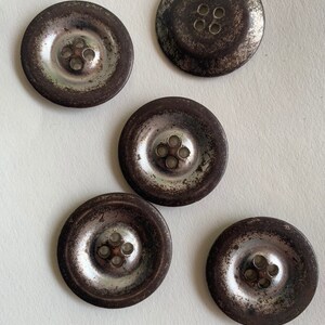May include: Five silver metal buttons with four holes each. The buttons have a worn, aged look with a dark brown patina.