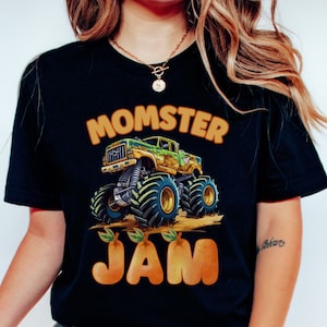 woman model is wearing a black t-shirt with the words "Momster Jam" with a green muddy Monster Truck. Jam Letters are Pear Gold Peachy Colored and shaped.  Personalized any Name Family Matching Monster Truck Jam Pit Party Theme.