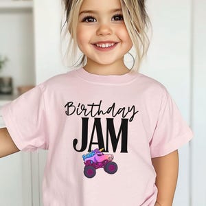 Personalized Name Girls Monster Truck Jam Sparkle Unicorn Smash Tee. Little girl is wearing a pink t-shirt that says "Birthday Jam" with a Unicorn Monster Truck with Rainbow Colors in Pink, Purple and Blue Colors. Cartoon style Big Truck with Birthday in Cursive Handwriting and Jam in Big Bold Letters in Black.