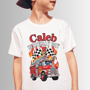 May include: White t-shirt with a red fire truck graphic, flames, and checkered flags. The text "Caleb Birthday Boy 3" is printed on the shirt.